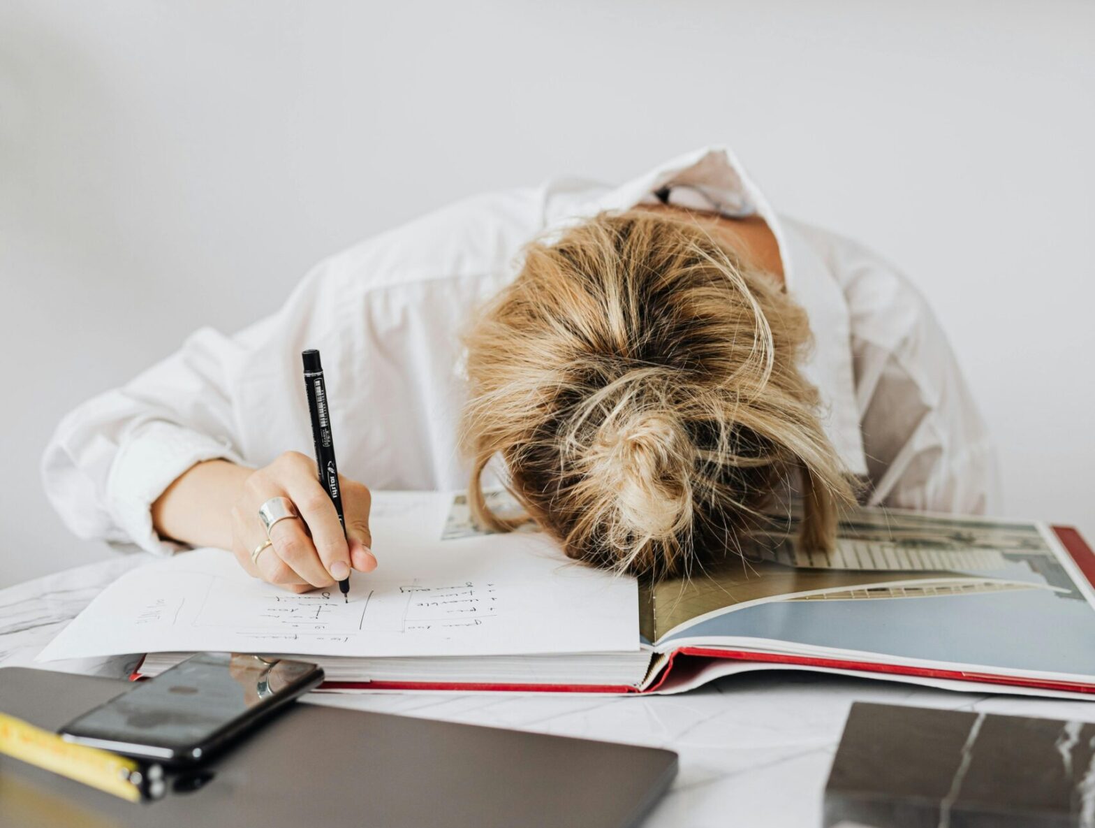 Women working at a desk with her head down and her pen still writing.